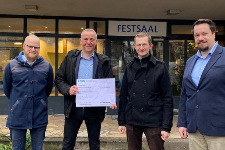 Vier Männer steht vor Festsaal mit Check