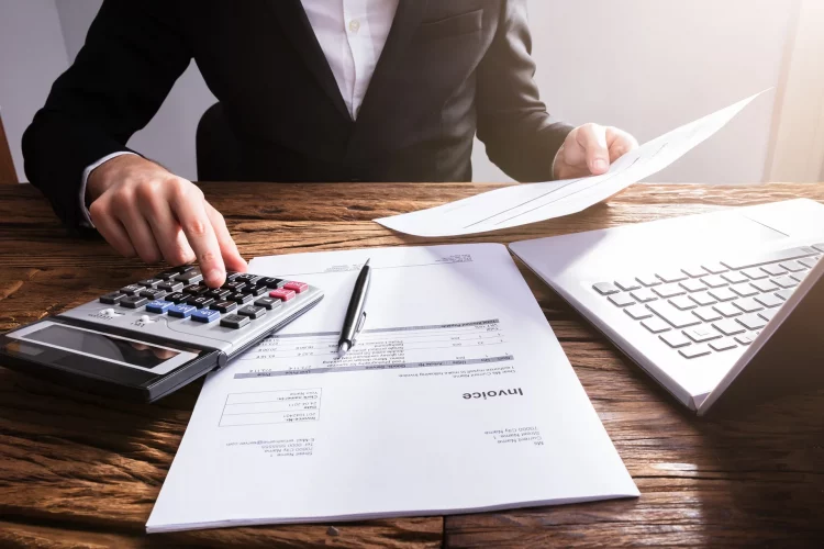 Die Hand eines Geschäftsmannes berechnet die Rechnung mit einem Laptop auf einem Holzschreibtisch