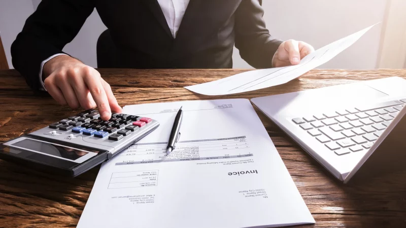 Die Hand eines Geschäftsmannes berechnet die Rechnung mit einem Laptop auf einem Holzschreibtisch