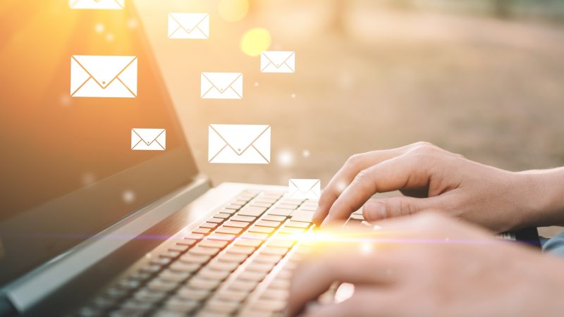 Frauenhand mit Tastatur-Laptop im Naturpark-Hintergrund im Freien mit E-Mail-Symbol, das abstrakt fliegt. Technologieunternehmen und freiberufliches Arbeitskonzept. Farbstil mit Vintage-Tonfiltereffekt.