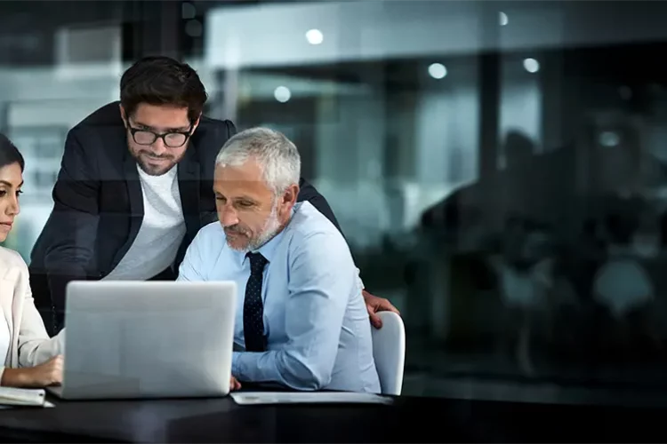 Das Business Team aus 3 Personen sitzt vor einem Laptop und bespricht Verträge