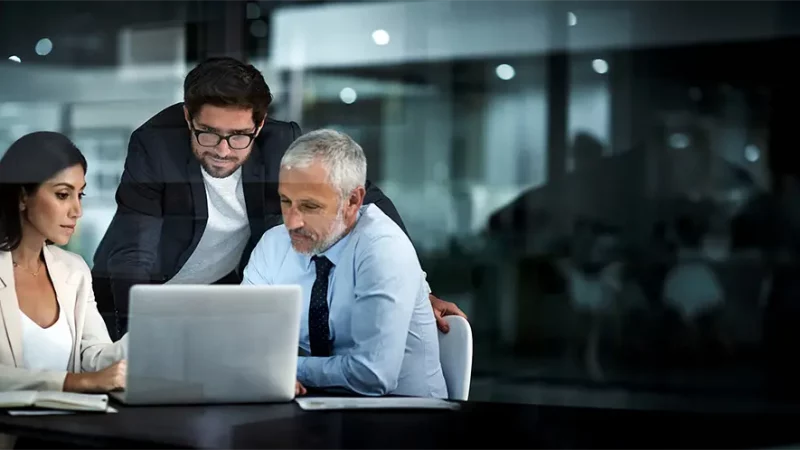 Das Business Team aus 3 Personen sitzt vor einem Laptop und bespricht Verträge