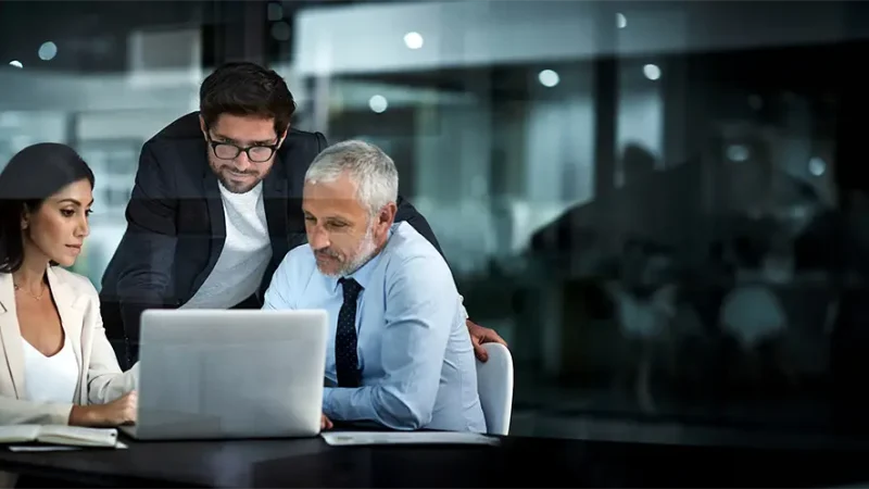 Das Business Team aus 3 Personen sitzt vor einem Laptop und bespricht Verträge