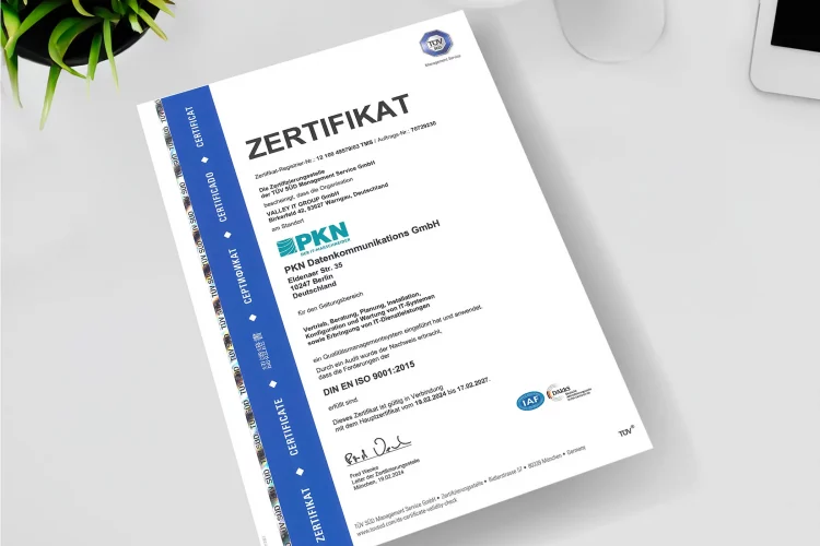 Blatt Papier mit TÜV Süd Zertifizierung auf einem Schreibtisch von der Vogelperspektive
